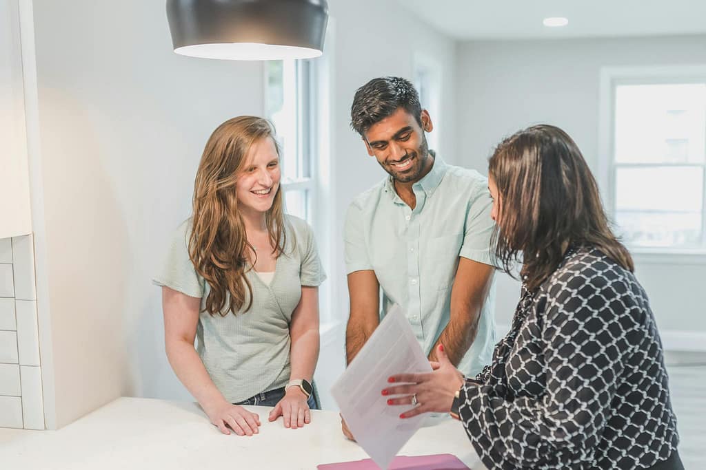 A smiling couple discusses real estate options with an agent inside a modern home.