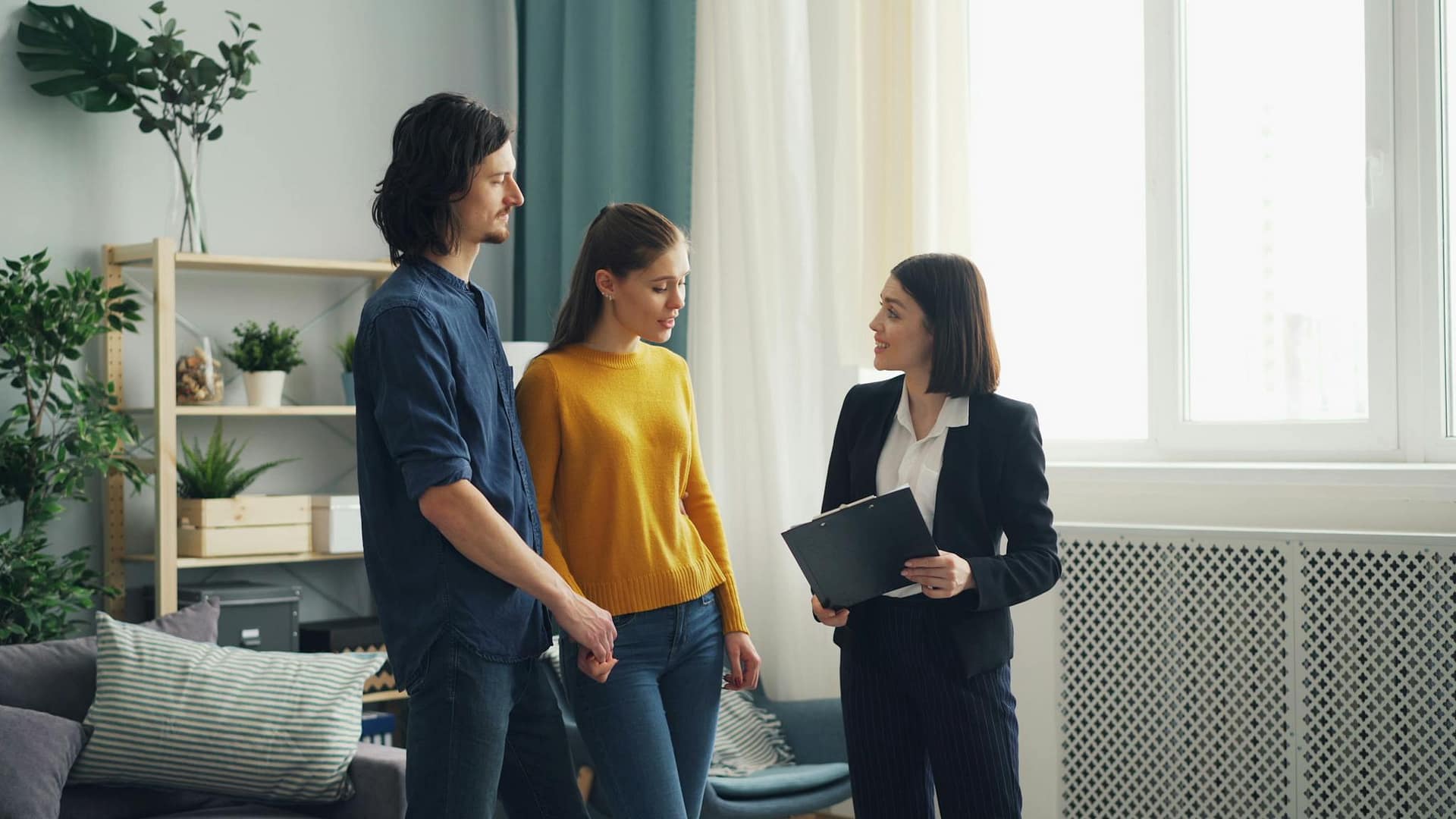 A young couple consults a real estate agent inside a modern living room, evaluating property options.